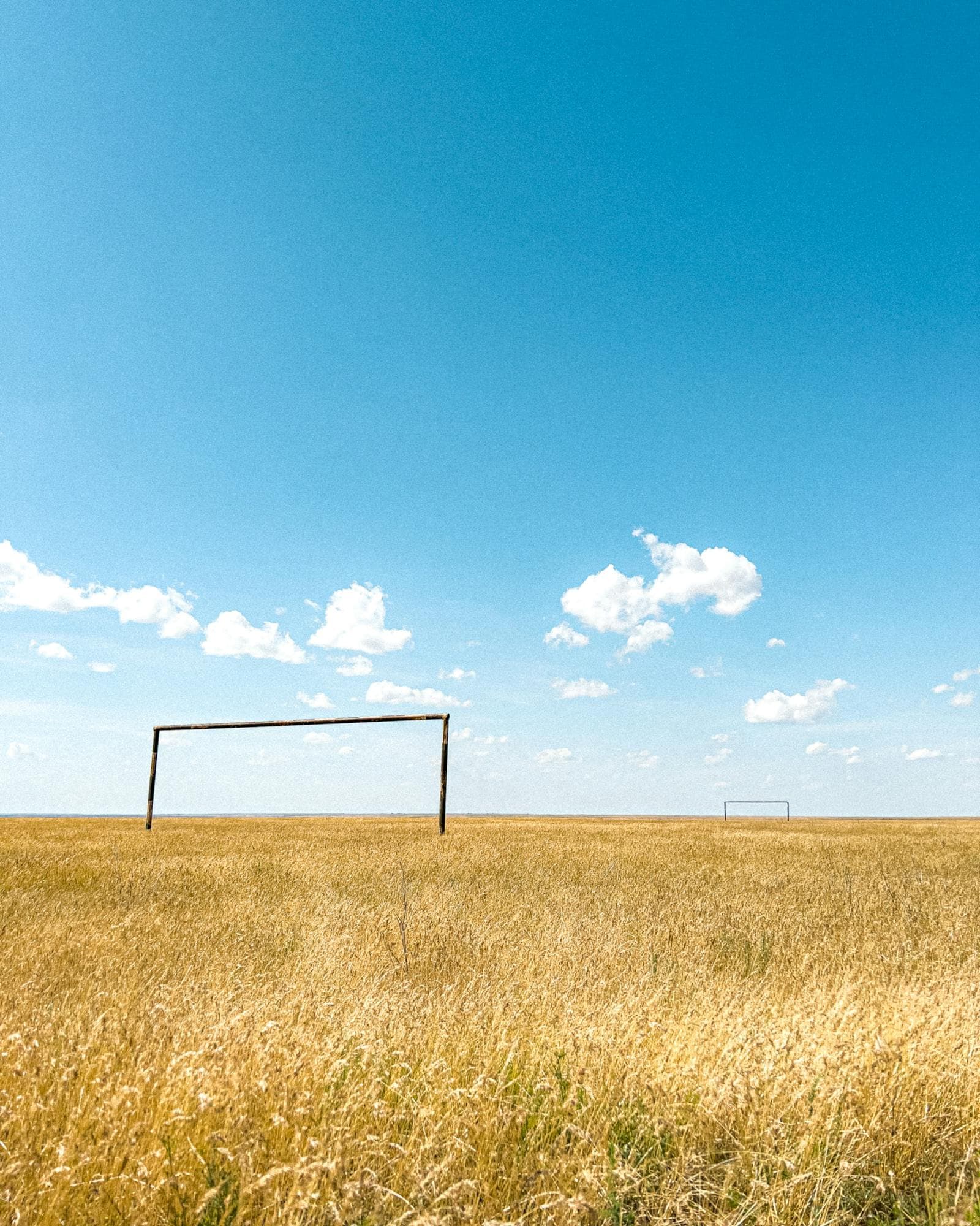 Goal frames standing in a wide, open grassroots pitch under a bright summer sky.
